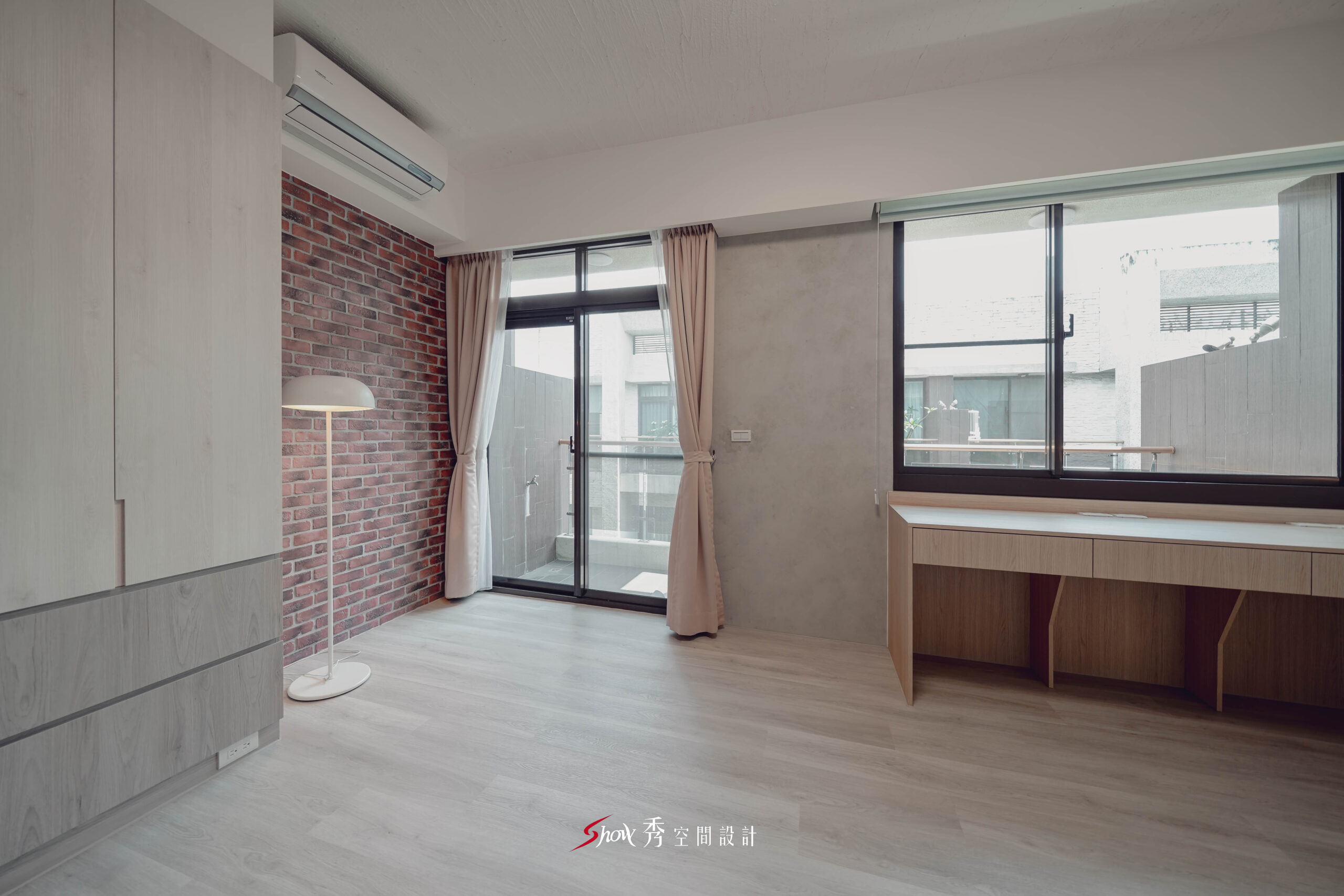 台南善化區透天老屋翻新主臥空間，配置窗邊長桌、灰色牆面、落地窗與紅磚造型牆，展現簡約又有層次的臥室設計。