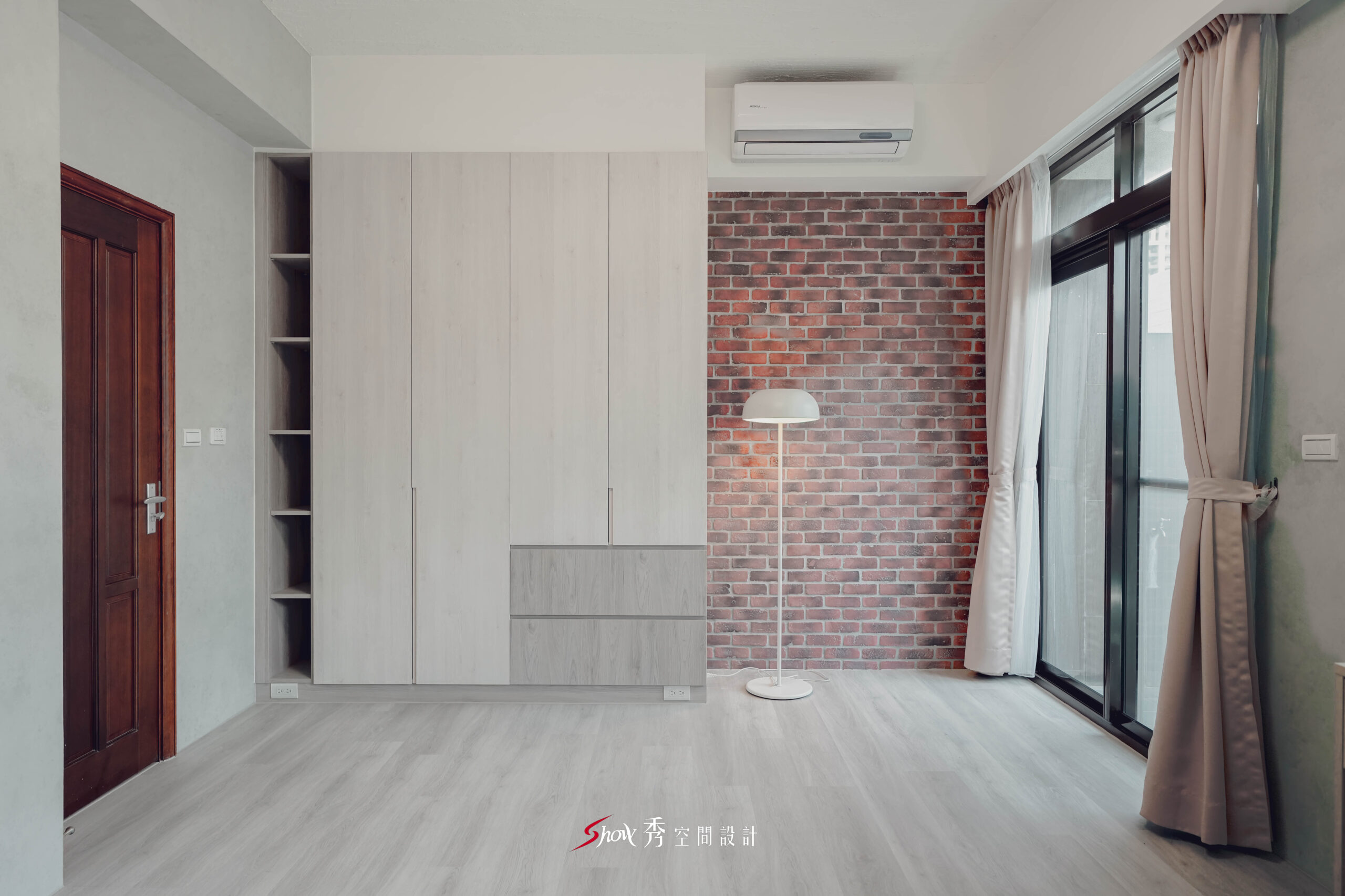 台南善化區透天老屋翻新主臥空間，以淺木紋系統衣櫃搭配紅磚造型牆與落地窗簾，展現現代簡約混搭輕工業風格。