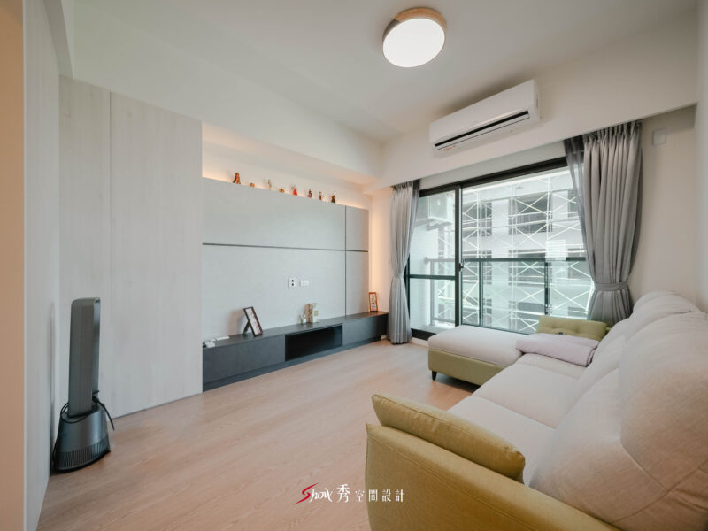 台南室內設計客廳空間，灰階電視牆搭配淺木地板與L型沙發