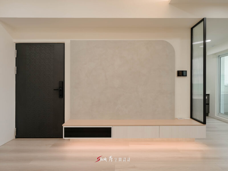 台南新市室內設計客廳，採用灰色弧形電視牆、淺木電視櫃、黑色大門與長虹玻璃隔屏，呈現現代簡約住宅風格。
