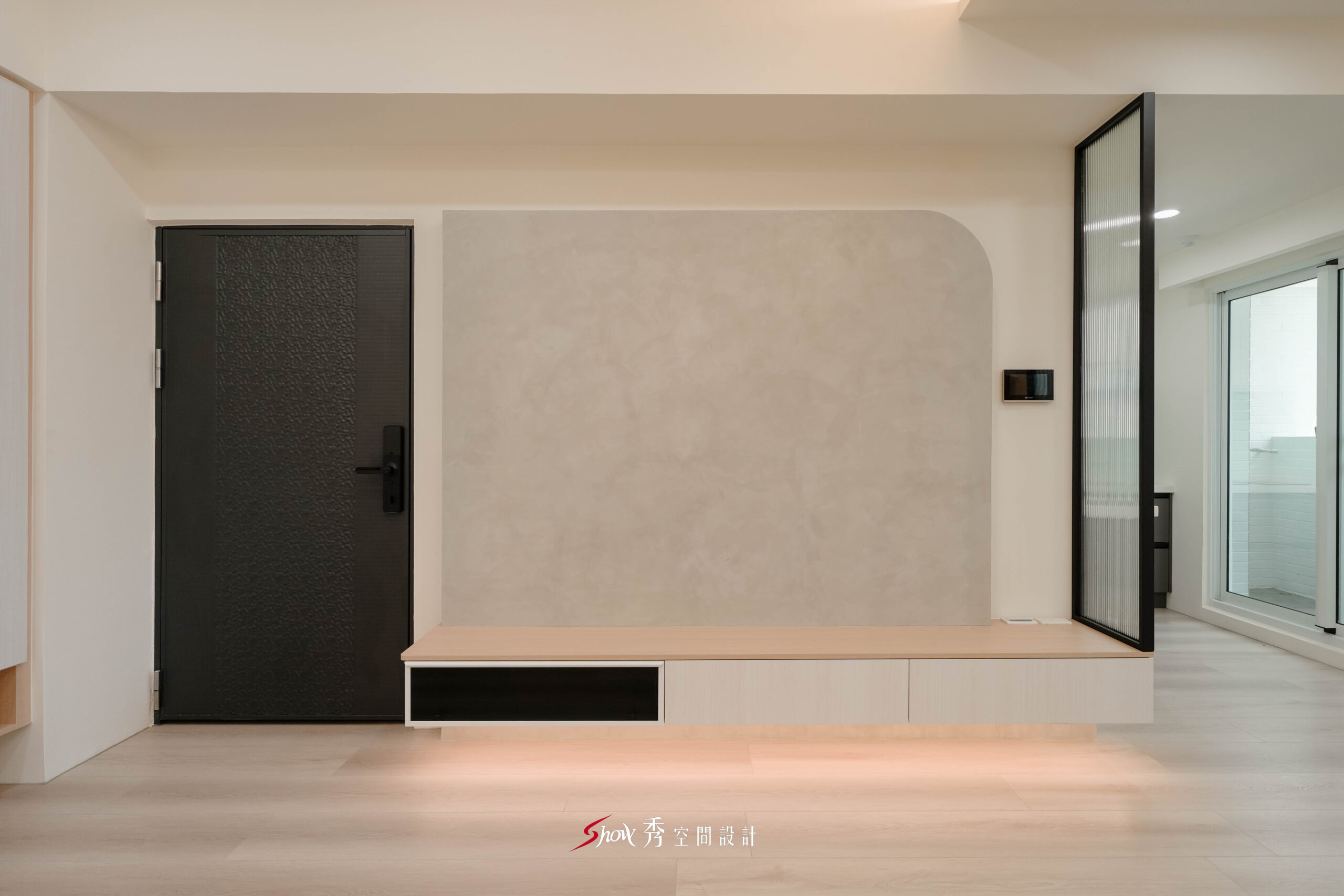 台南新市室內設計客廳，採用灰色弧形電視牆、淺木電視櫃、黑色大門與長虹玻璃隔屏，呈現現代簡約住宅風格。