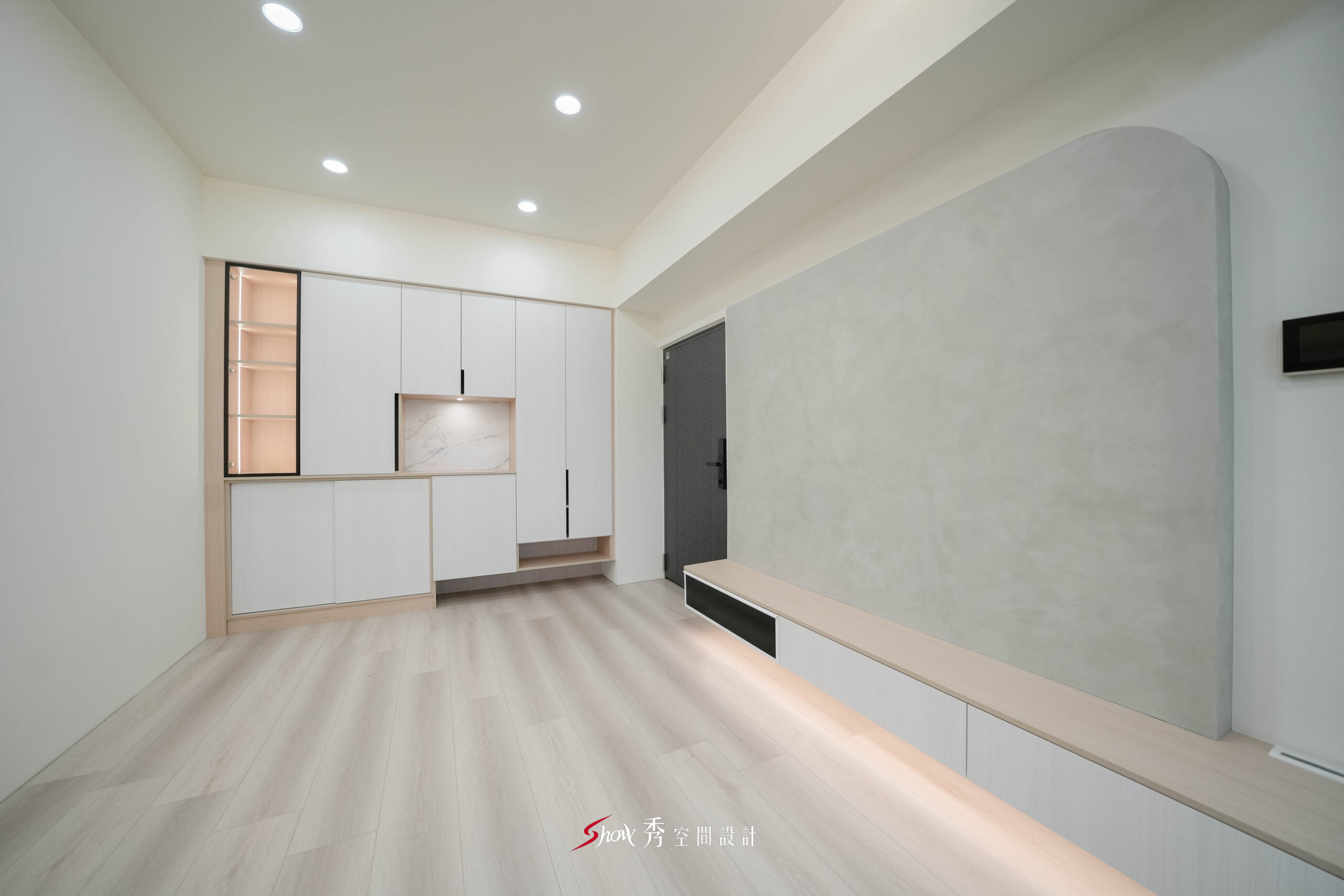 台南新市住宅客廳設計，灰色弧形電視牆搭配白色玄關收納櫃與淺木紋地板。