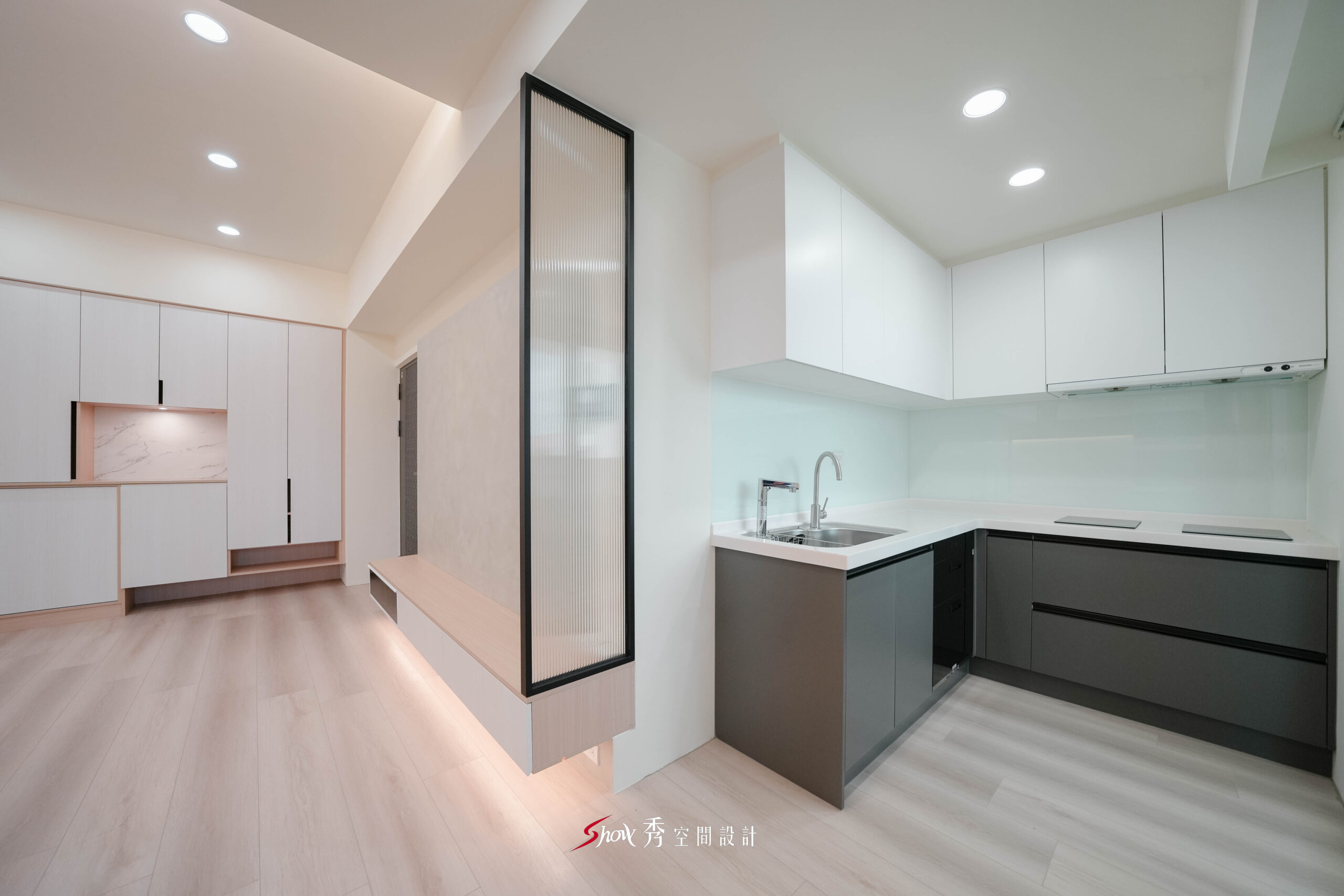 台南新市住宅設計，開放式廚房搭配長虹玻璃隔屏與灰黑色廚具，形成現代簡約風格。