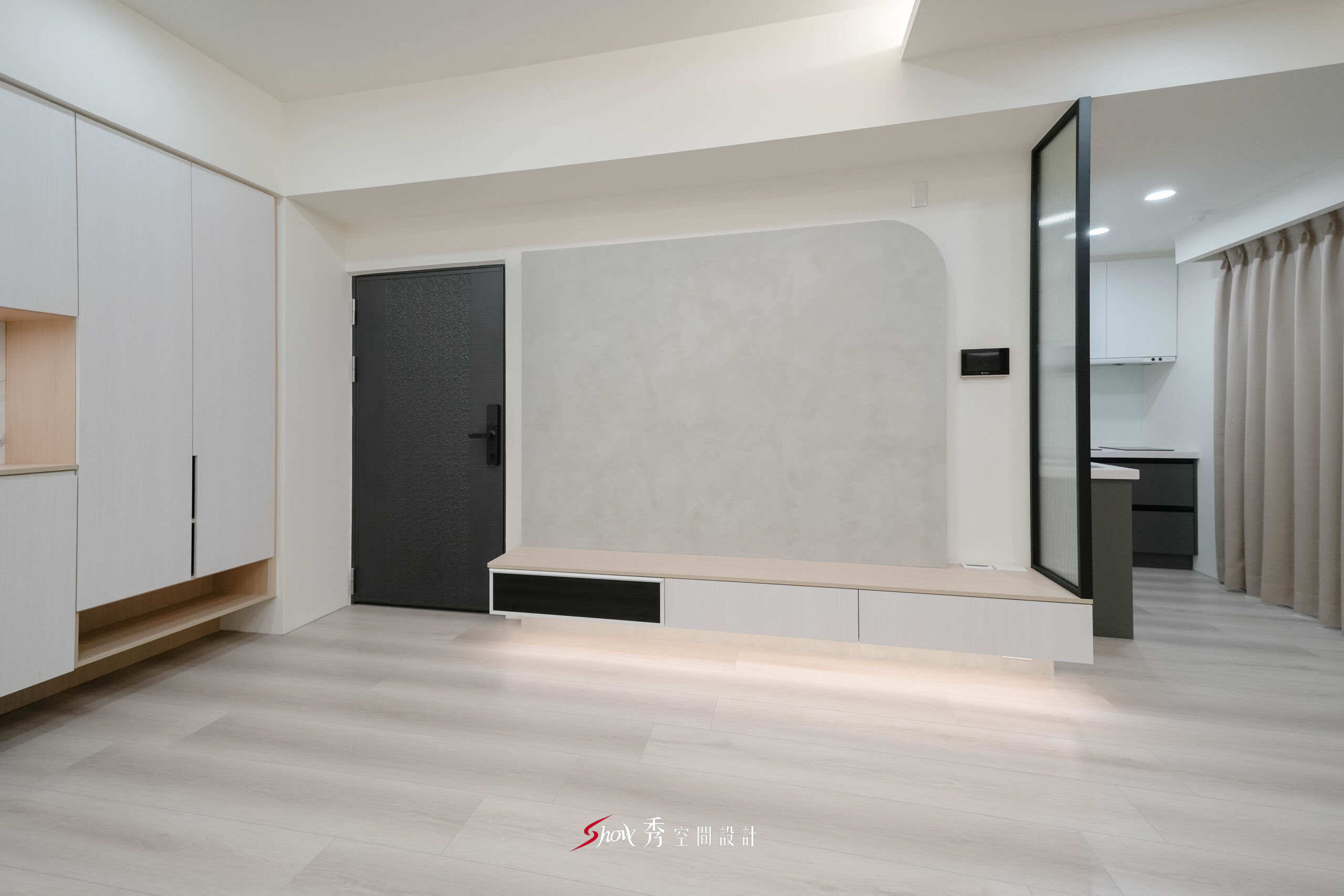 台南新市室內設計案，弧形灰色電視牆搭配懸浮電視櫃、長虹玻璃隔屏與開放式廚房。