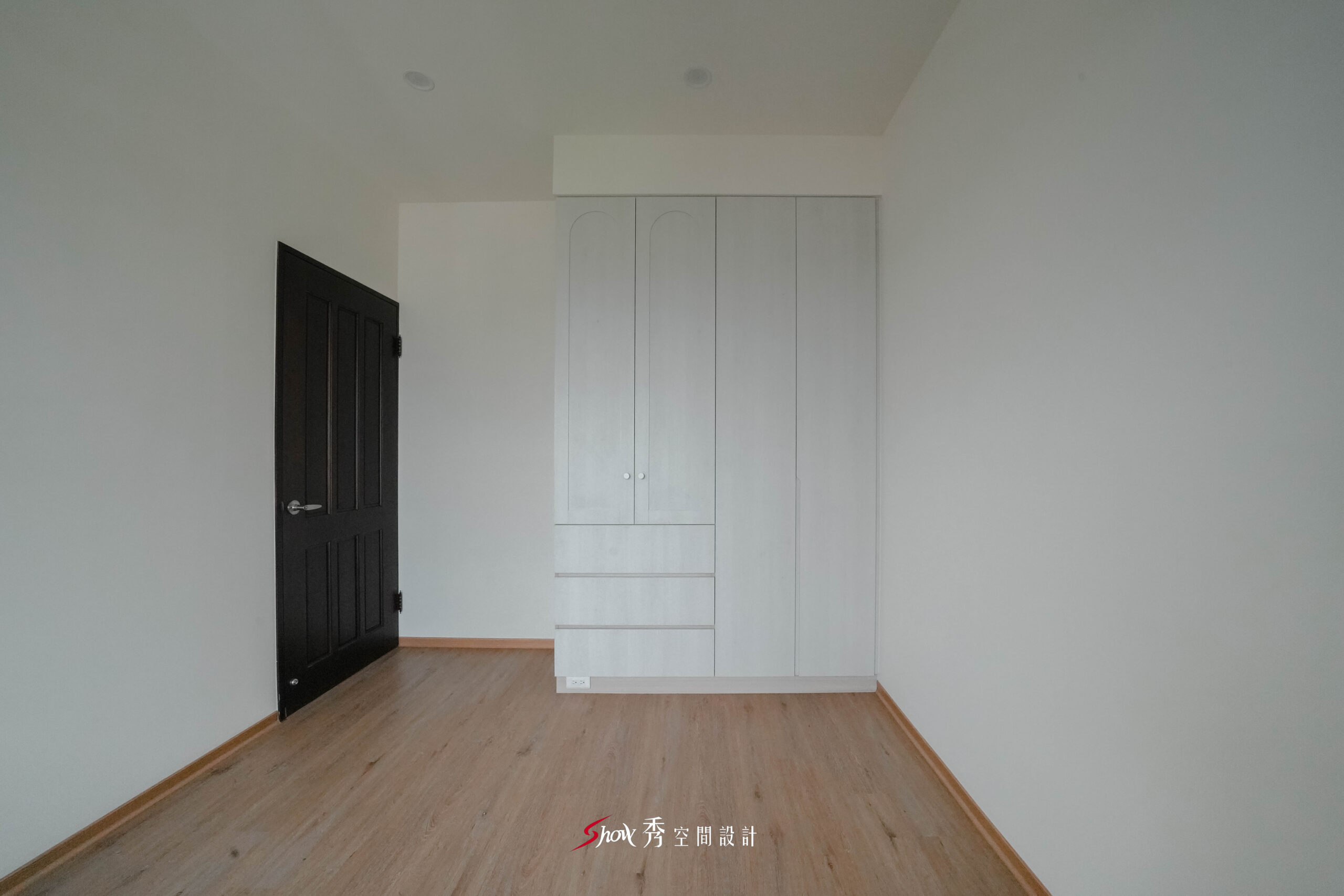 主臥空間採木地板搭配白色系統衣櫃與深色木門，呈現簡潔明亮的居家氛圍。