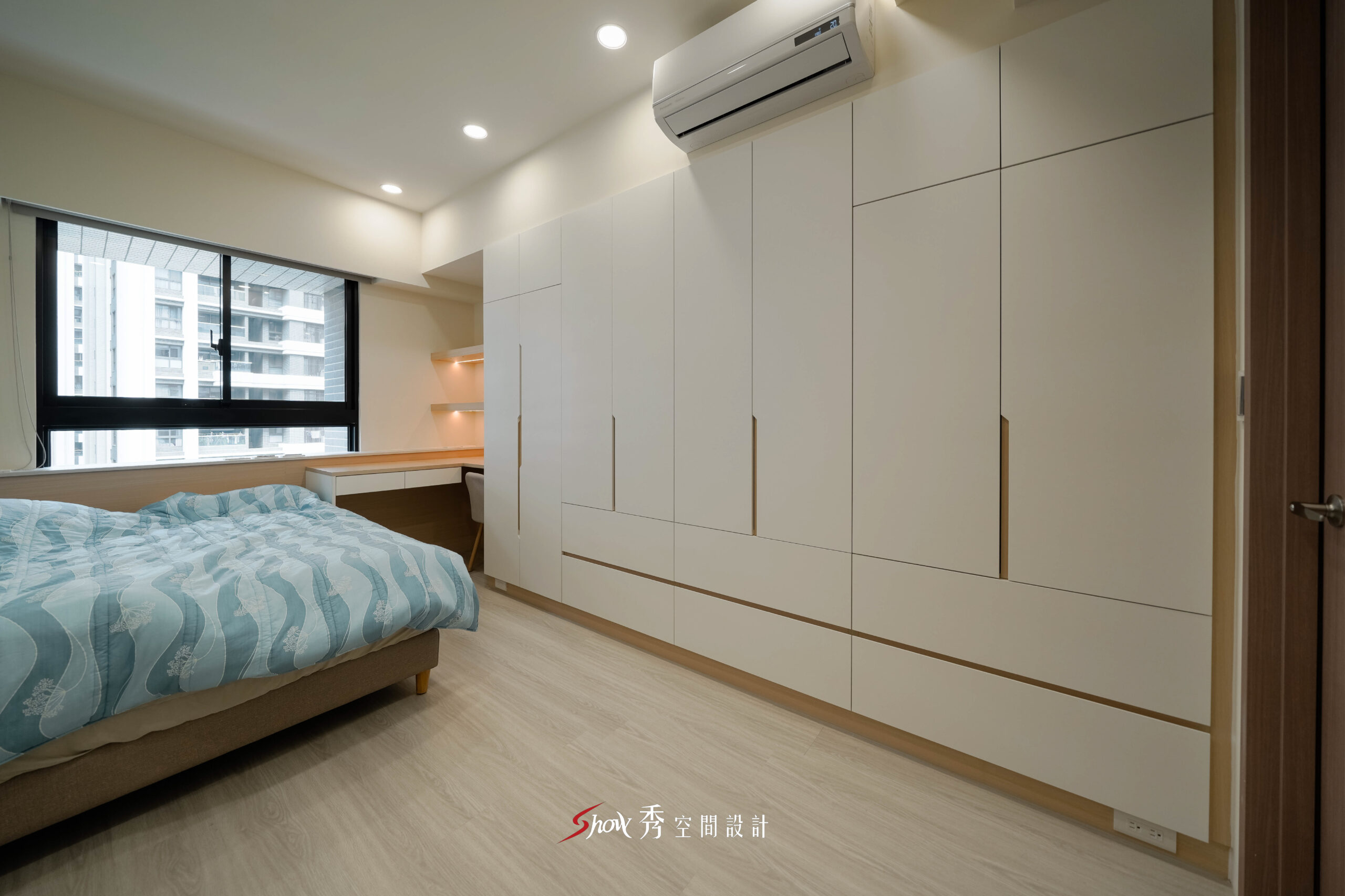台南主臥室設計，以白色系統衣櫃、木紋地板與窗邊書桌打造現代簡約風格。