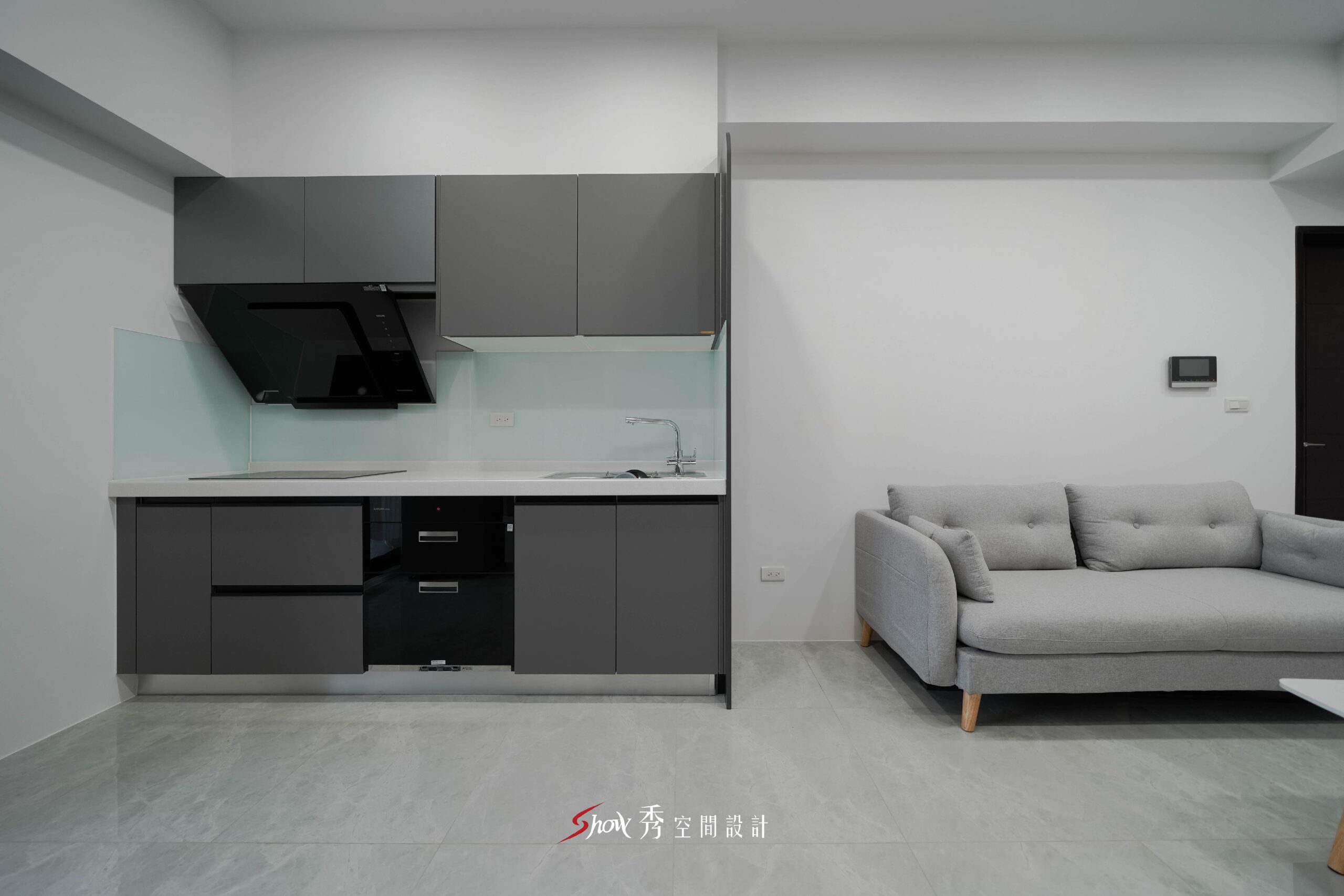 灰色一字型廚房與淺灰沙發相鄰配置的開放式公共空間設計