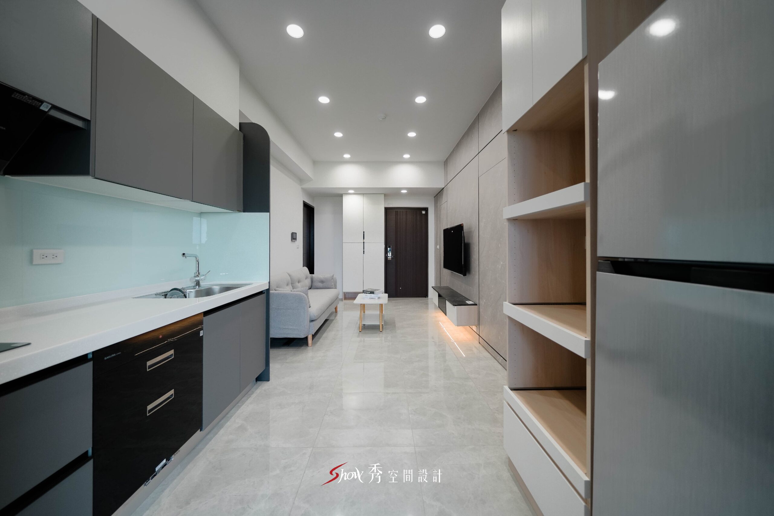 由廚房望向客廳的開放式空間設計，結合電視牆、收納展示櫃與淺灰色地坪